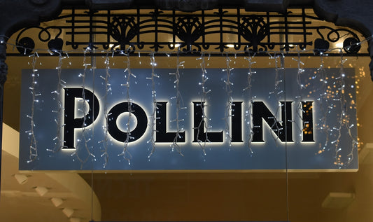 Insegna del negozio Pollini con decorazioni luminose, rappresentativa della storia delle borse iconiche.